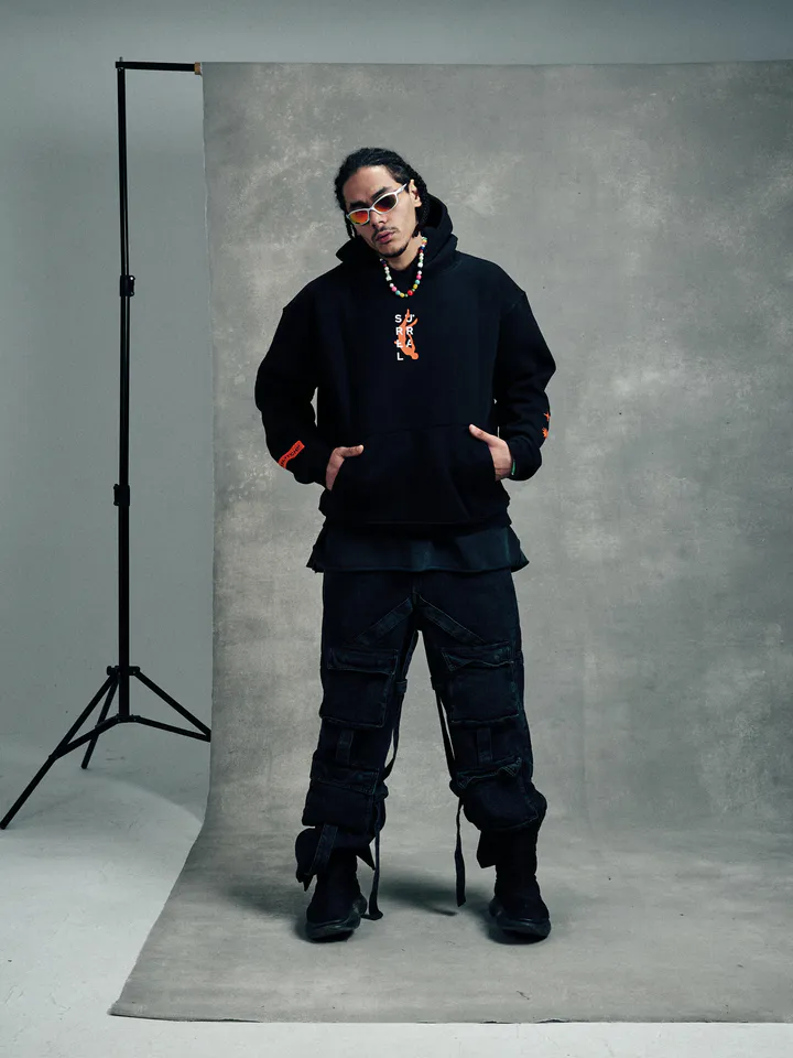 Model in sunglasses and a black hoodie standing in front of a grey studio backdrop, from the Glitch streetwear campaign
