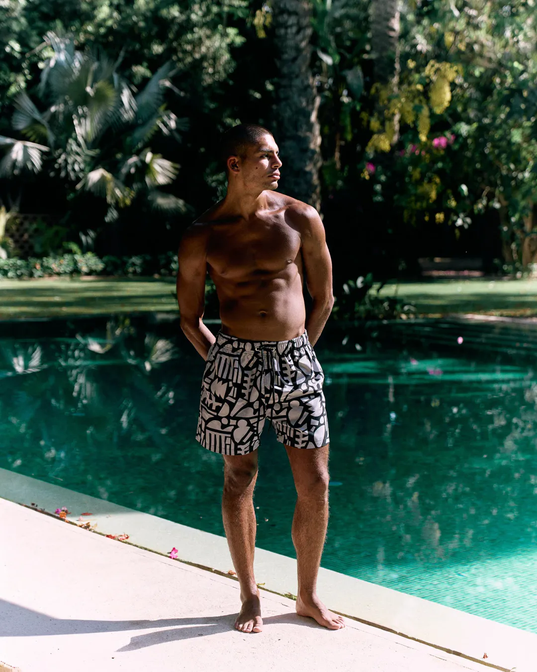 Man in patterned swim shorts standing beside a green pool